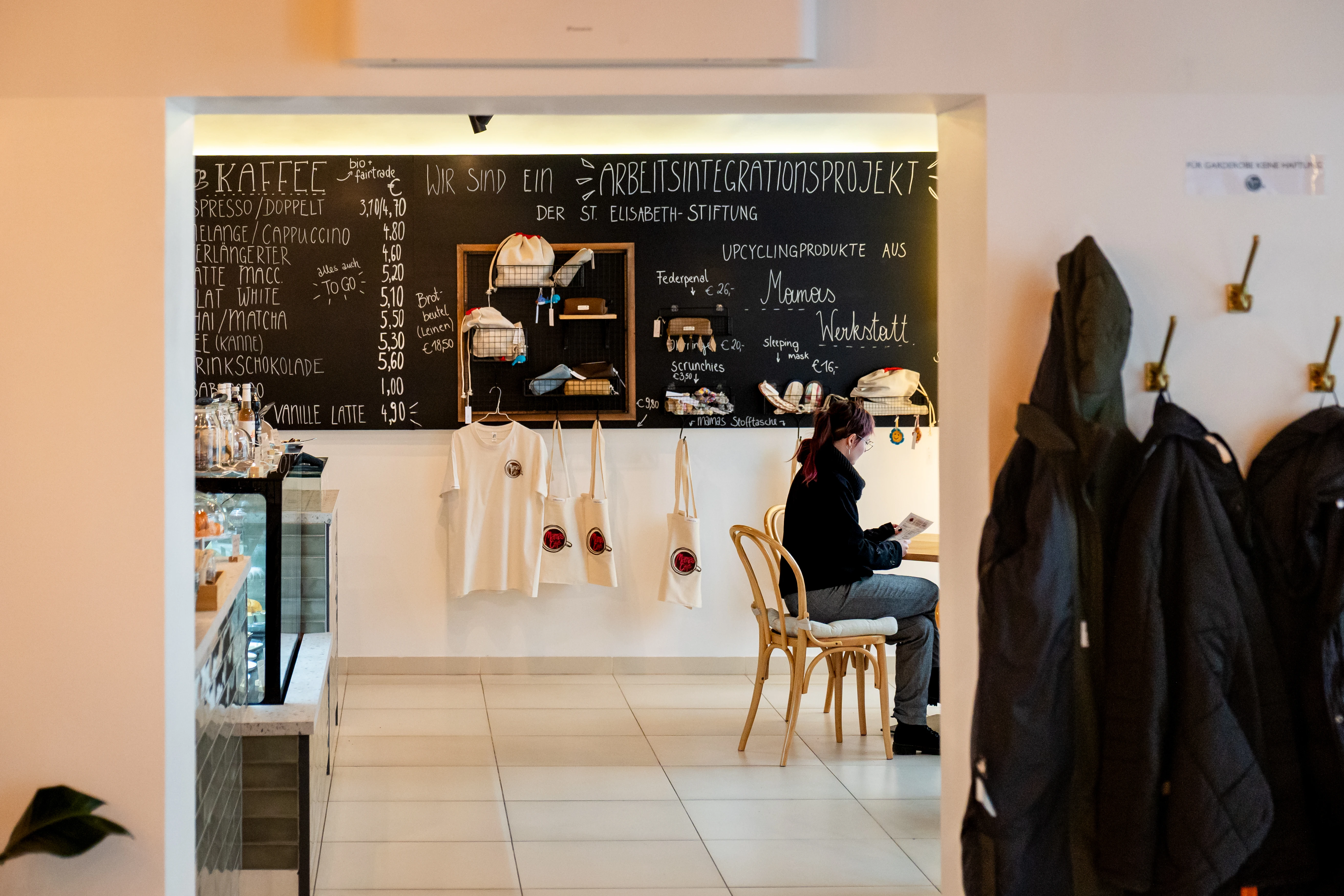 Bild von Stephan Schönlaub: Blick in ein Café, das ein Arbeitsintegrationsprojekt der St. Elisabeth-Stiftung ist.  Es sind eine Speisekarte, Upcycling-Produkte und eine Person sichtbar. © Erzdiözese Wien/Schönlaub